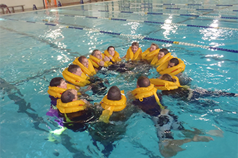 Company Training Program - A group of people inside a pool holding hands on a helicopter safety training.