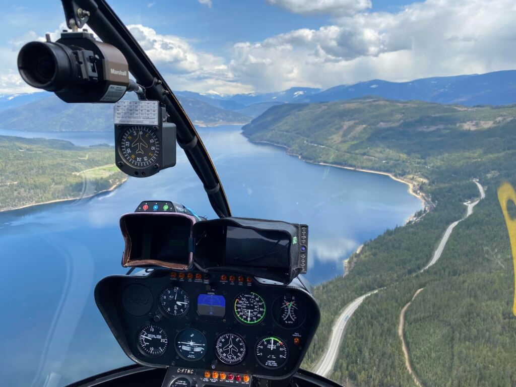 Robinson R44 cockpit POV flying over winding mountain lake — book custom helicopter tours in Calgary, Alberta with L R Helicopters