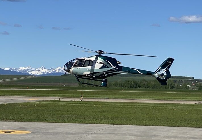 L R Helicopters EC120 taking off from Springbank Airport with the Rocky Mountains behind it