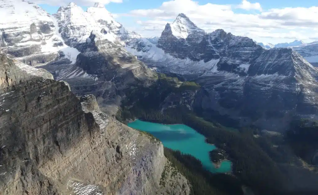 Aerial view of a turquoise glacial lake and snow-capped Rocky Mountain peaks on the Lake Louise Helicopter Tour with L R Helicopters