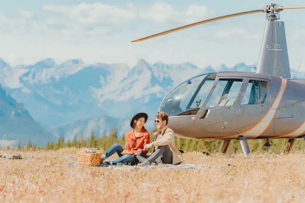 Couple picnicking beside an L R Helicopters aircraft on Jumpingpound Mountain in the Alberta Rockies on the Picnic on a Peak experience